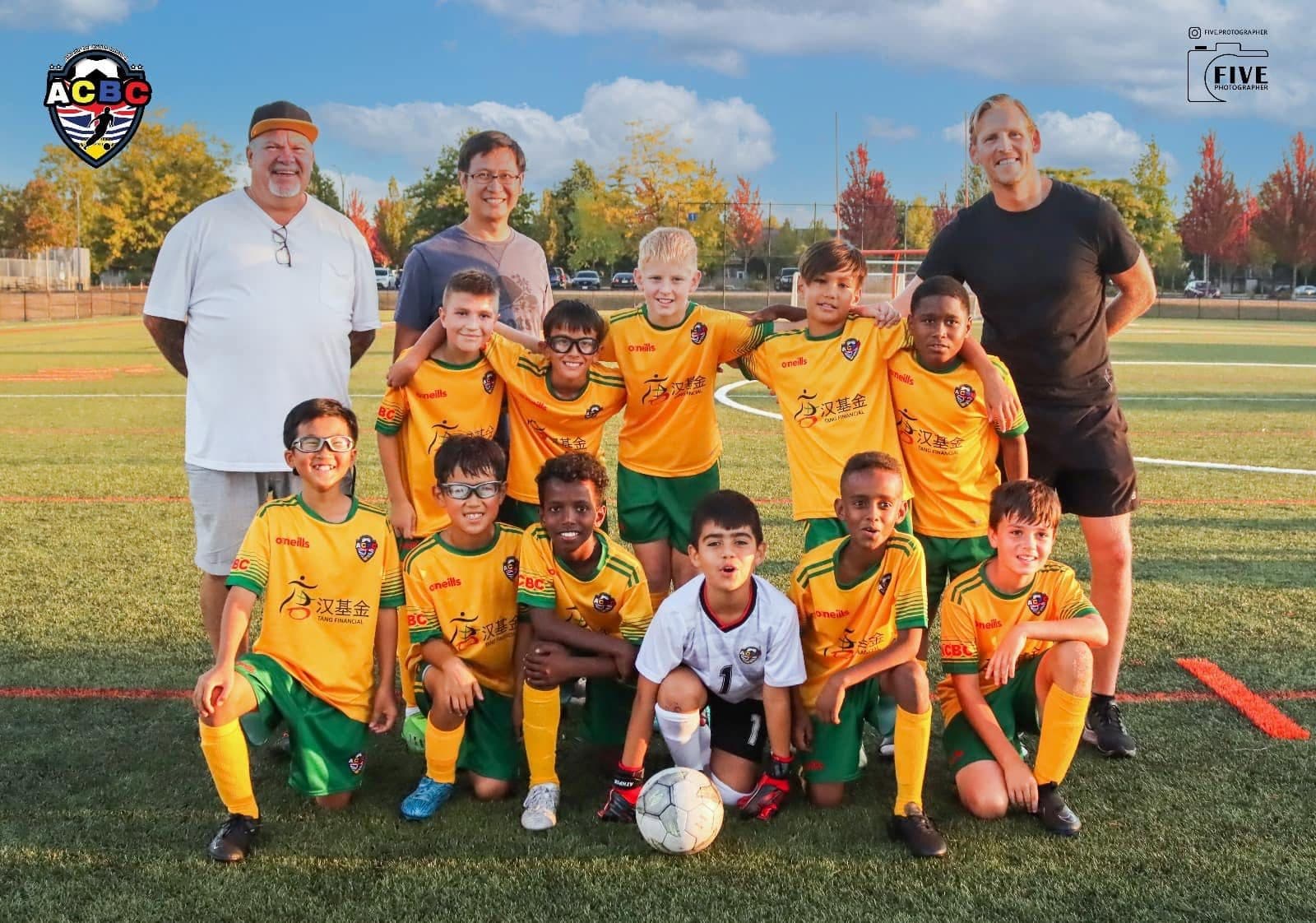 An ACBC youth squad and two coaches lined up on the pitch in the green and gold kit
